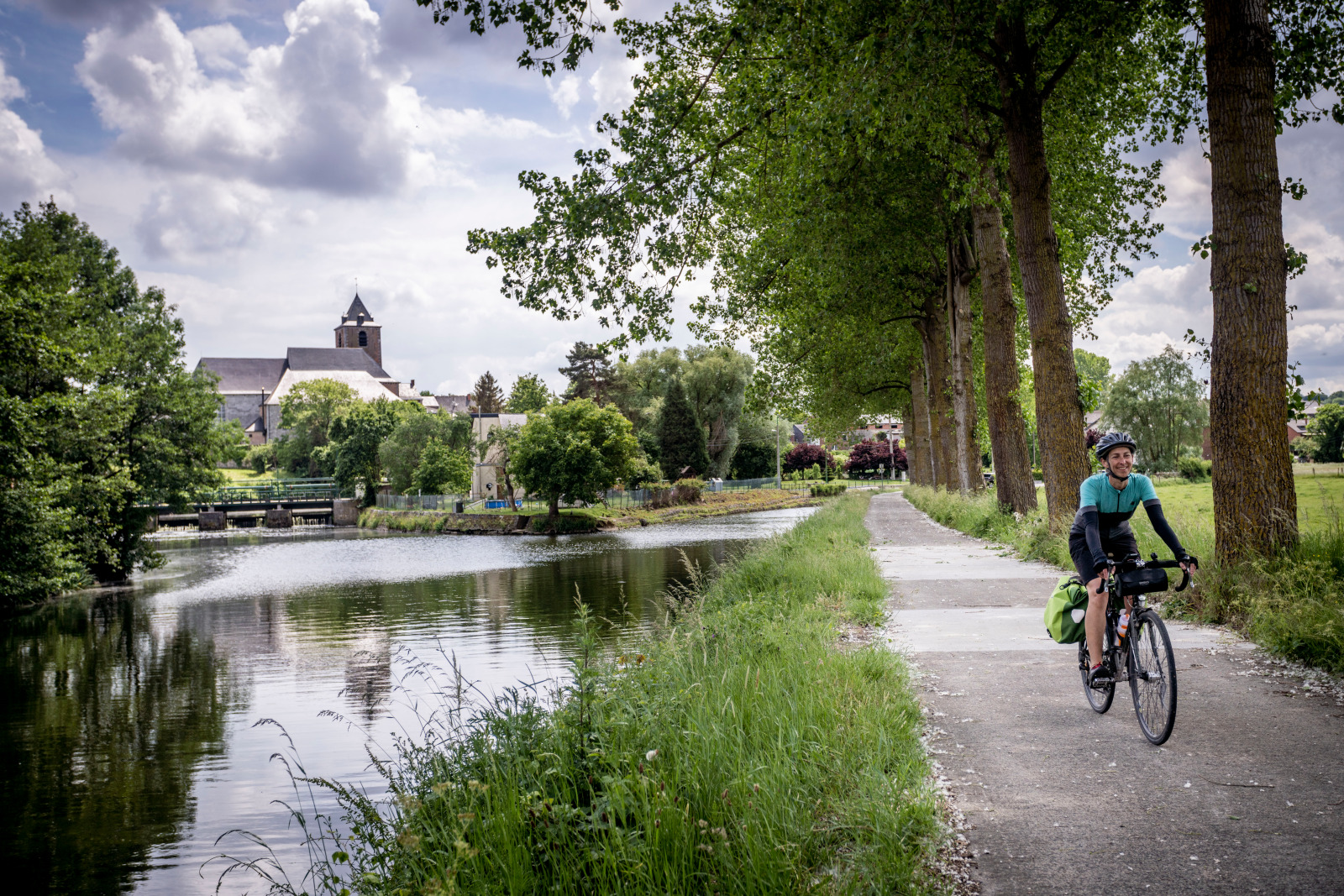 Cyclist along the water and view of the Saint-Médard church in Solre-sur-Sambre