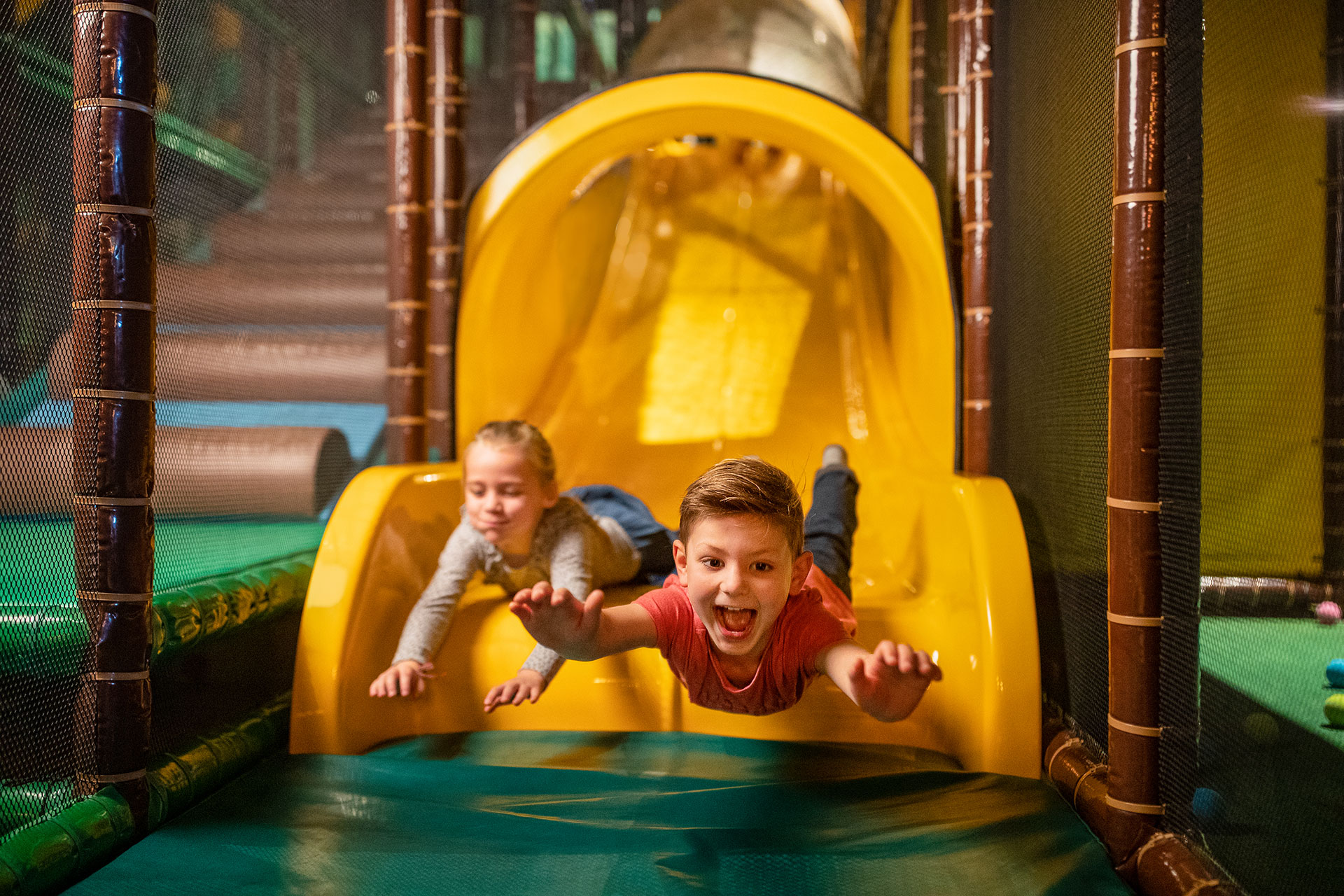 Een meisje en een jongen glijden van de glijbaan op het speelplein in Center Parcs Les Ardennes