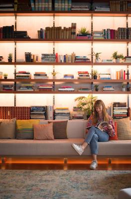Young woman reading a book in front of a large bookcase in the lobby of the Yust Hotel in Liège